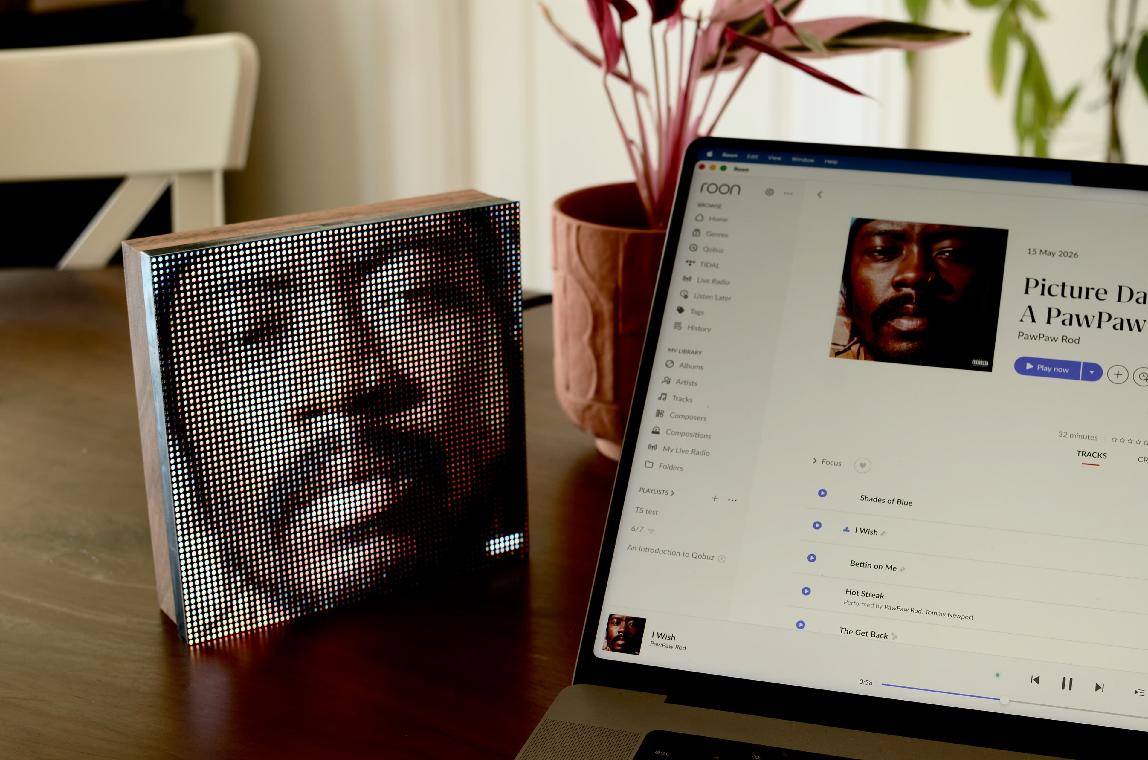 Tuneshine on a bedside table showing album art while a phone displays the same track in Roon